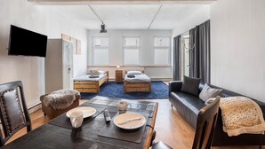 Una sala moderna con un sofá, una mesa de comedor con platos y cubiertos, y dos camas sobre una alfombra azul.