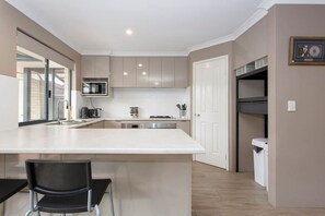 Una cocina moderna con una isla central, electrodomésticos integrados y una zona de comedor con una silla.