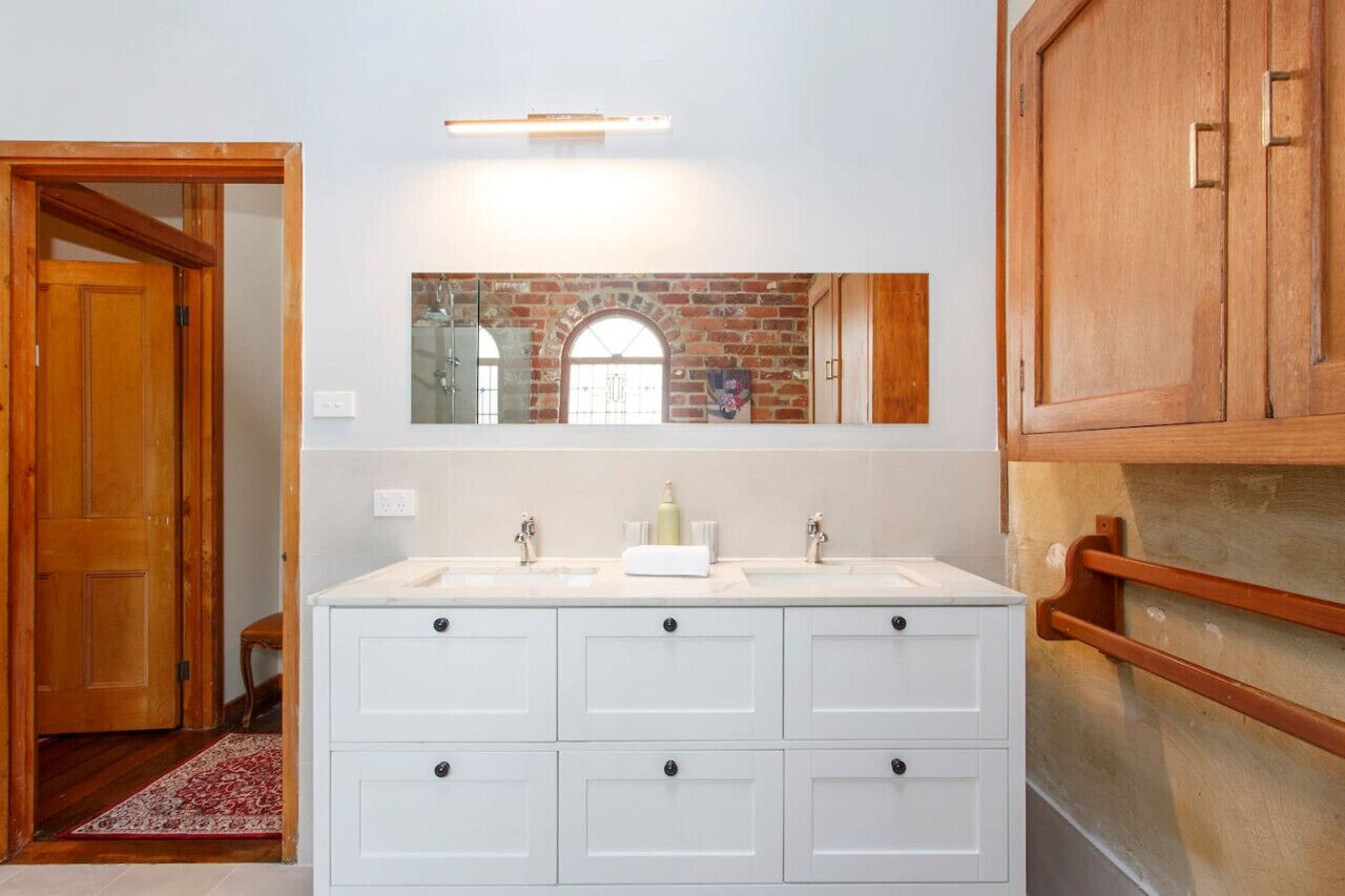 A bathroom with a white vanity, two sinks, a mirror, and a wooden door.