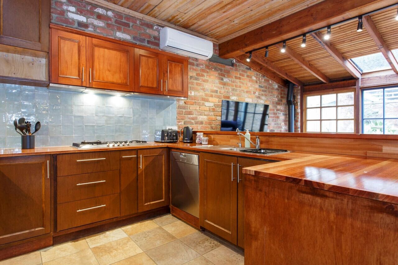 Een keuken met houten kastjes, een bakstenen muur en een groot raam.