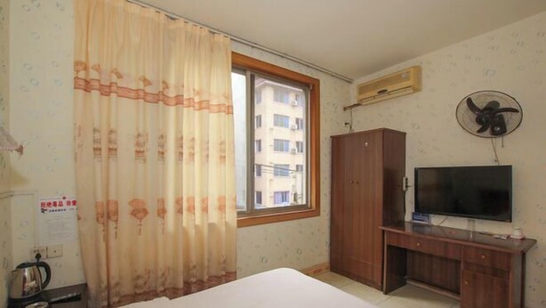 Hotelkamer met een bed, een bureau met televisie, een kledingkast, een raam met gordijnen en een airconditioning.