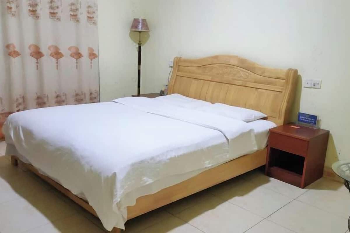 A single bed with a wooden headboard, a nightstand with a lamp, and a curtain with a floral pattern.