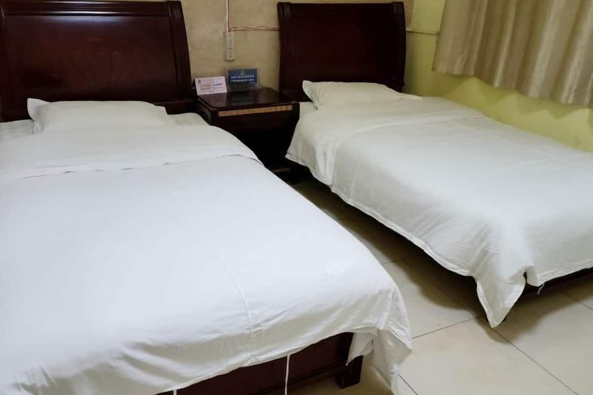 A hotel room with two single beds, wooden headboards, a nightstand, and a wall socket.