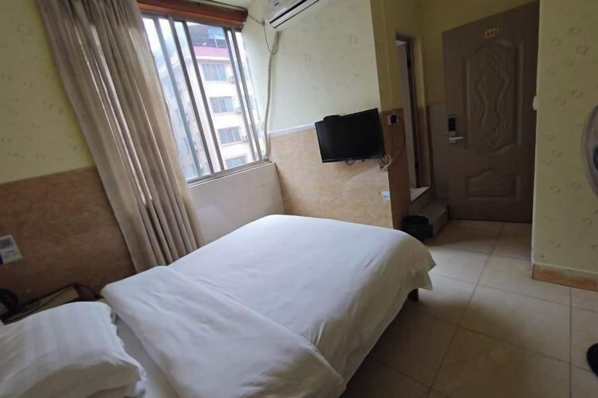 A hotel room with a bed, a TV mounted on the wall, a window with curtains, and a door.
