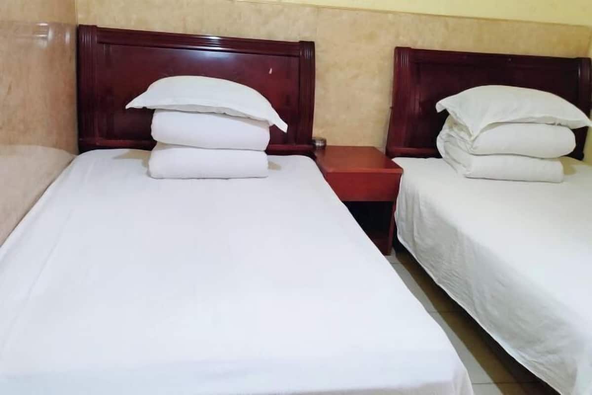 A hotel room with two single beds, each with white linens and pillows, and a wooden headboard.