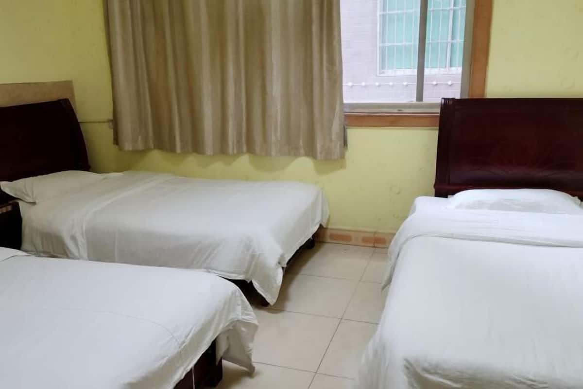 A room with three single beds, a window with curtains, and a view of the street outside.