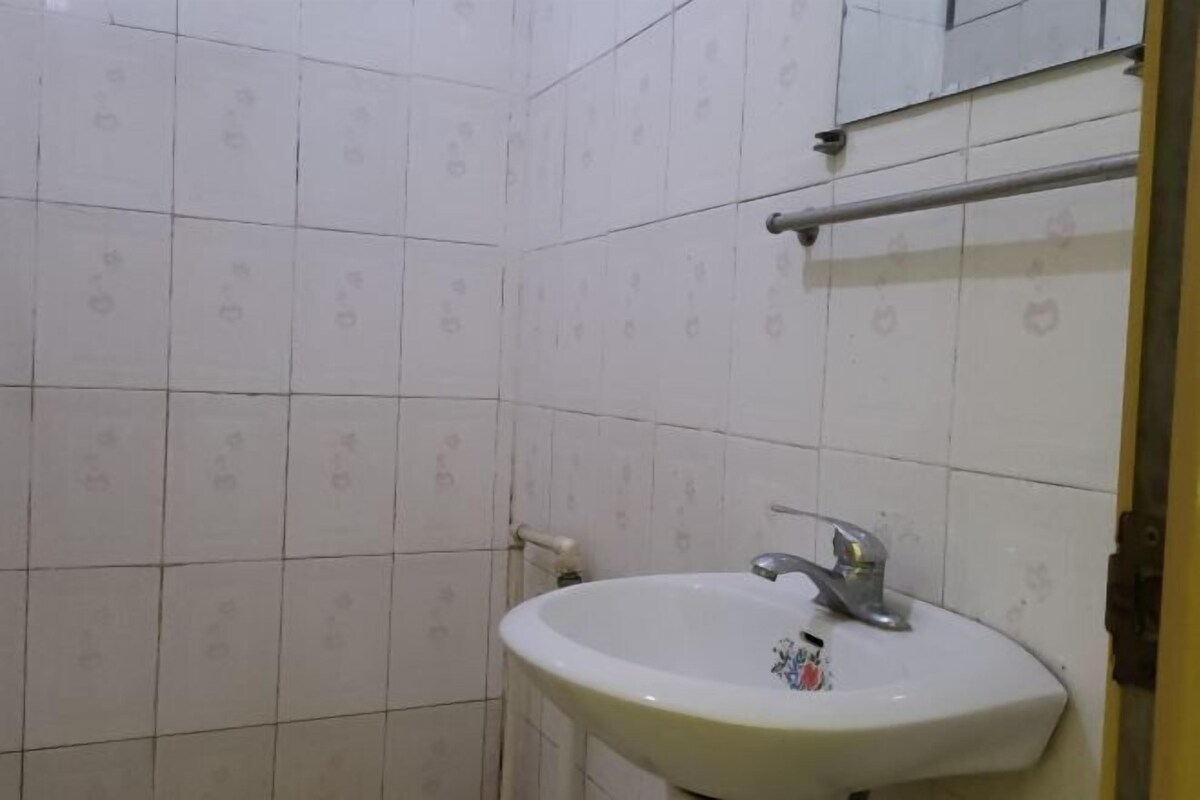 Un baño con paredes de azulejos blancos y un lavamanos blanco con grifo.