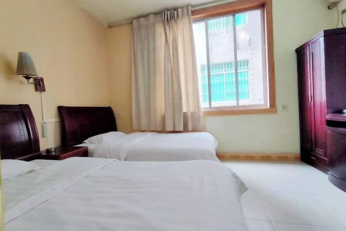 A hotel room with two beds, a window with curtains, a lamp, and a wardrobe.