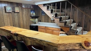 A bar area with a wooden bar top, bar stools, and a staircase leading to a seating area. - Stepaway Vacation Rentals- Crazy Loon Lodge (St.Germain)
