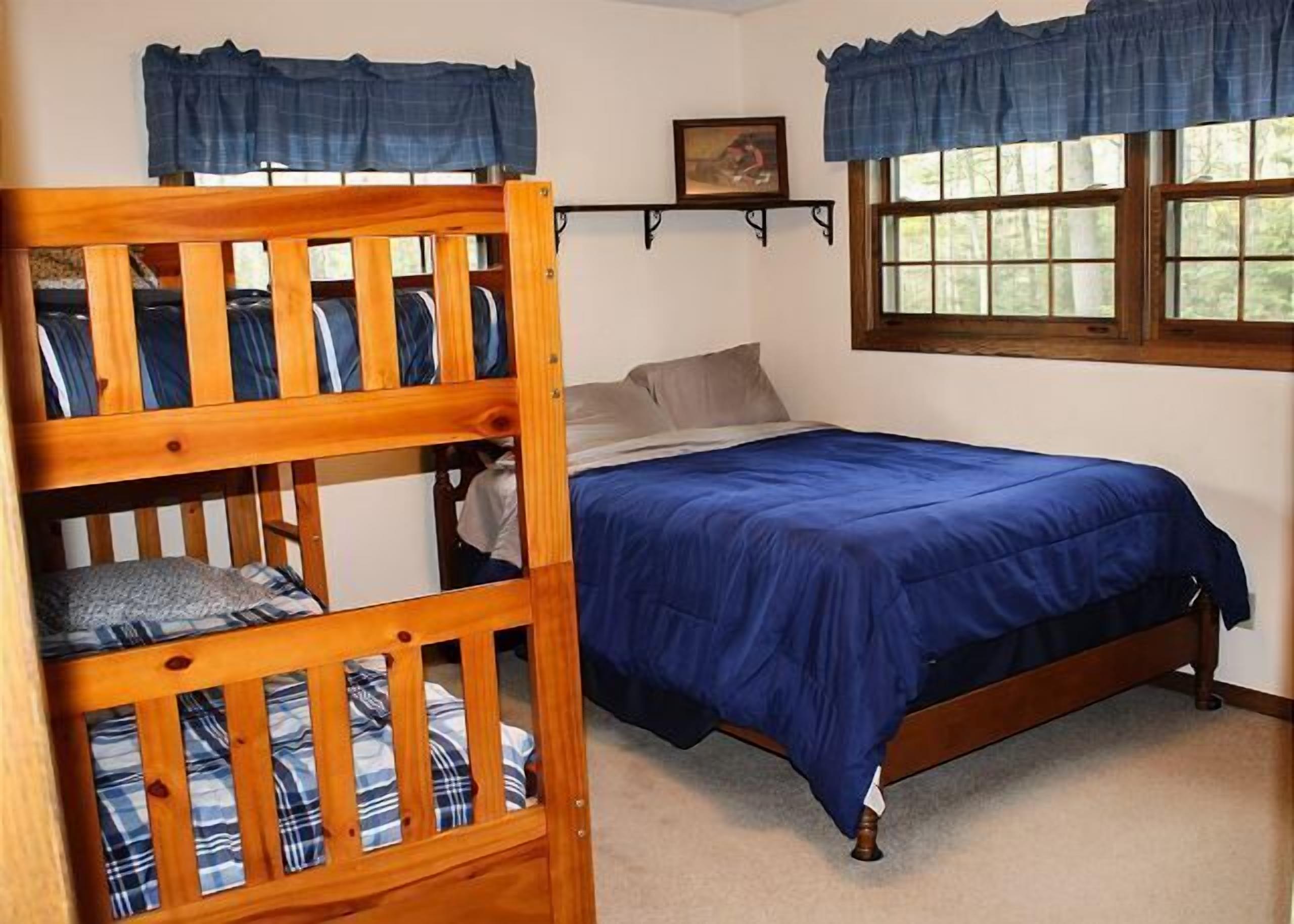 Un dormitorio con una cama litera, una cama individual, una ventana con cortinas, un cuadro en la pared y una estantería.
