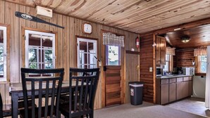 A wooden cabin interior with a dining area, kitchen, and a clock on the wall. - Stepaway Vacation Rentals- Cla-Rie Cabin (St.Germain)
