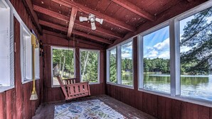 A wooden cabin with large windows overlooking a lake, a ceiling fan, and a patterned rug on the floor. - Stepaway Vacation Rentals- Cla-Rie Cabin (St.Germain)