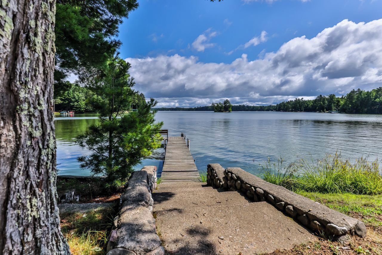 A wooden pier leading to a calm lake surrounded by trees and a clear sky.