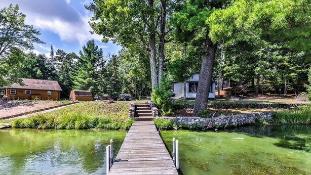 A wooden dock leading to a house surrounded by trees and a small pond. - Stepaway Vacation Rentals- Cla-Rie Cabin (St.Germain)