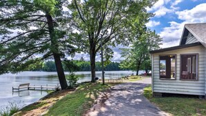 A lakeside cabin with a paved path leading to a dock, surrounded by trees and a grassy area. - Stepaway Vacation Rentals- Cla-Rie Cabin (St.Germain)