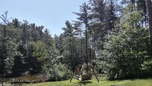 Un espacio cubierto de césped con un arenero de madera y un estanque al fondo.
