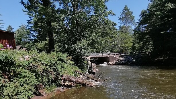 Un muelle de madera que se adentra en un río, con un puente al fondo.