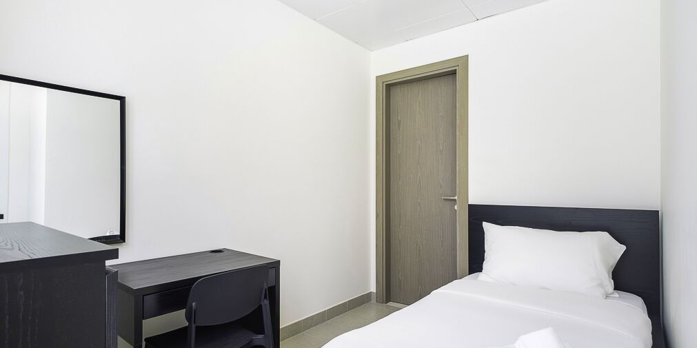 A hotel room with a bed, a desk, a chair, and a door.