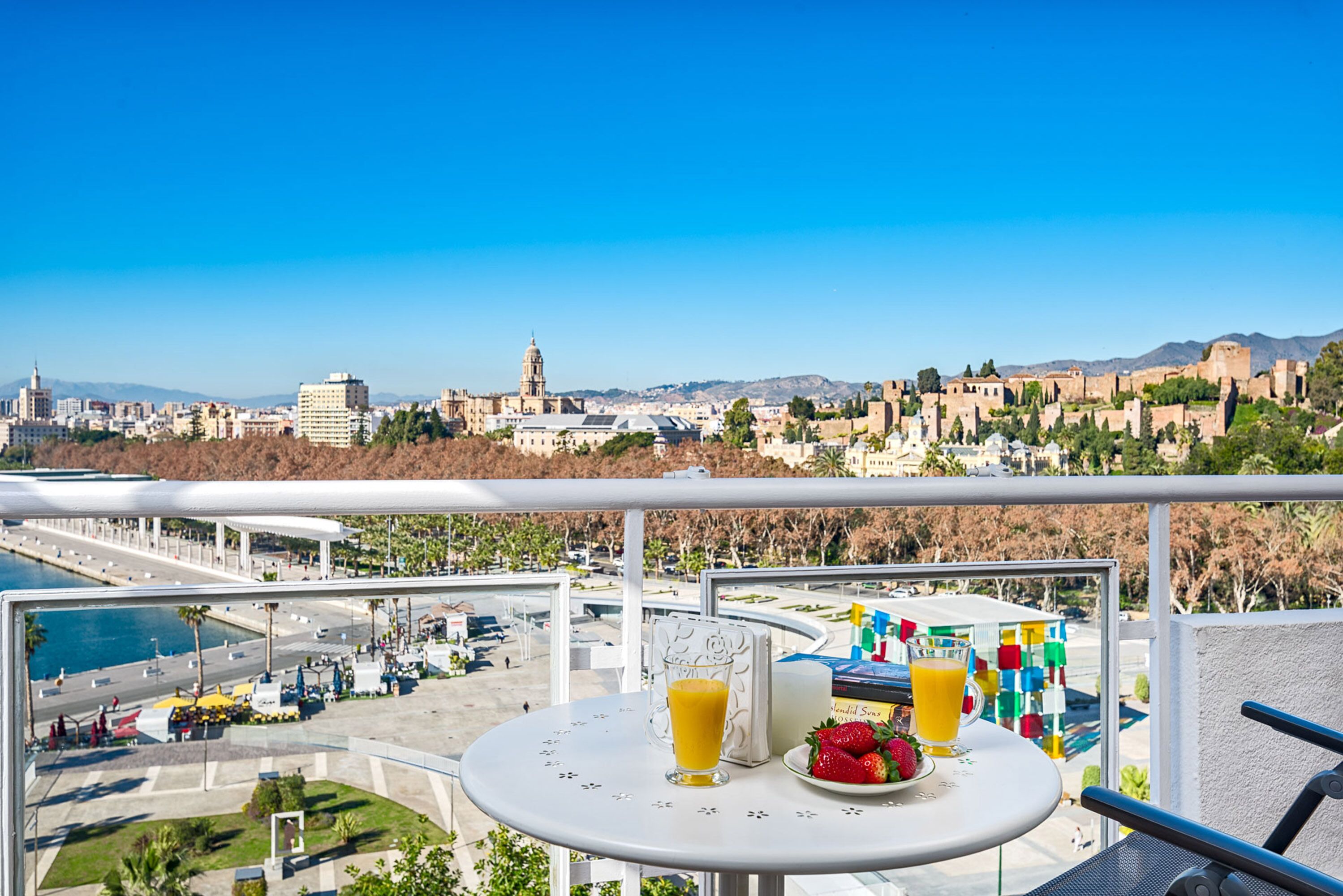 A balcony with a table set for two, overlooking a cityscape with historical buildings and a clear blue sky.