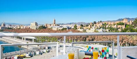 A balcony with a table set for two, overlooking a cityscape with historical buildings and a clear blue sky.