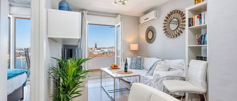 Una sala moderna con un sofá, una mesita de centro y una estantería. Hay un ventanal con vistas a un paisaje urbano.