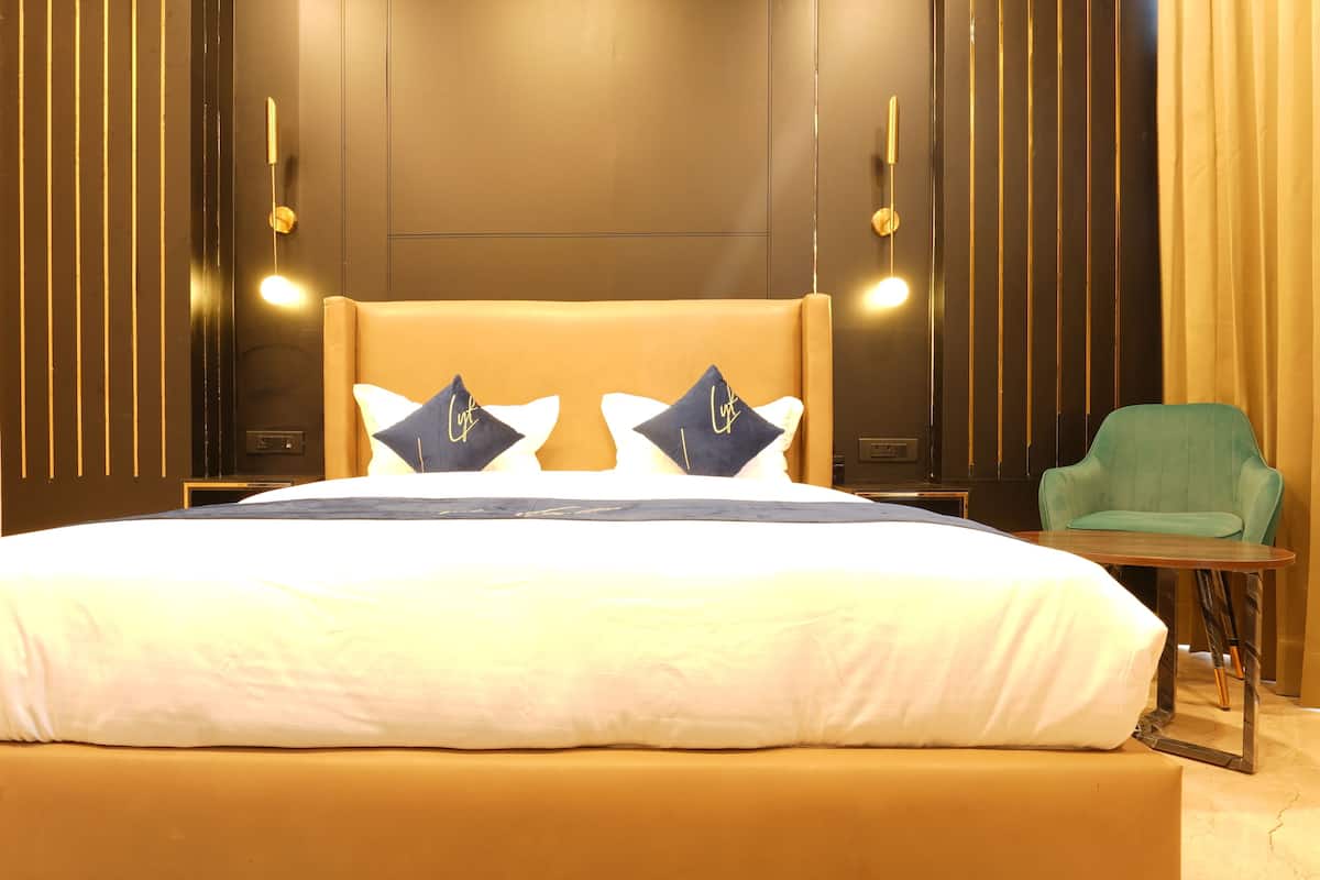 A hotel room with a large bed, two bedside tables, a green armchair, and a dark wooden headboard.