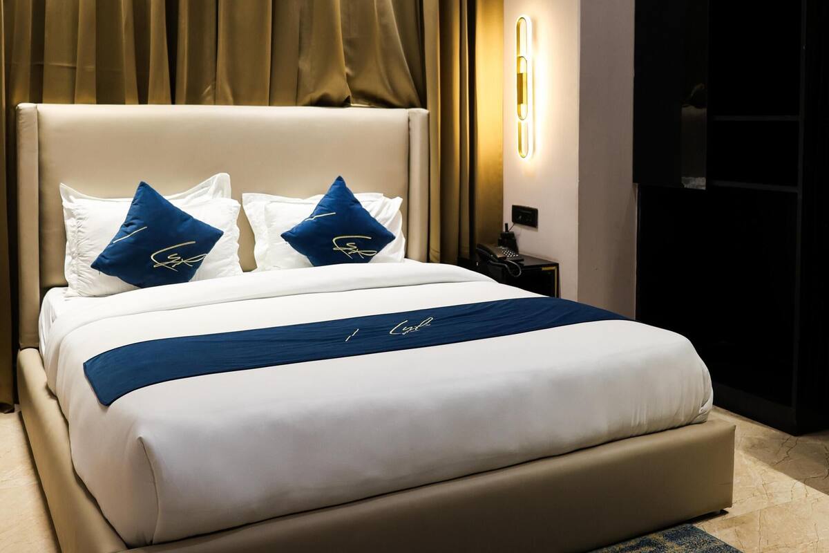 A hotel room with a large bed, a nightstand, a TV, and a wall-mounted light.
