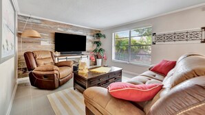 A modern living room with a leather sofa, a recliner, a flat-screen TV, and a wooden accent wall. - Family Retreats 5 minutes to the beach (Tarpon Springs)