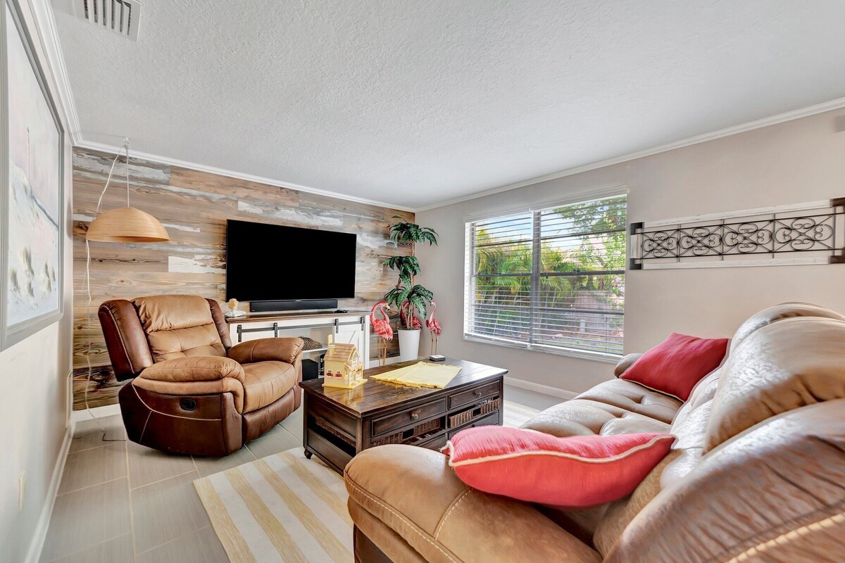 A modern living room with a leather sofa, a recliner, a flat-screen TV, and a wooden accent wall.