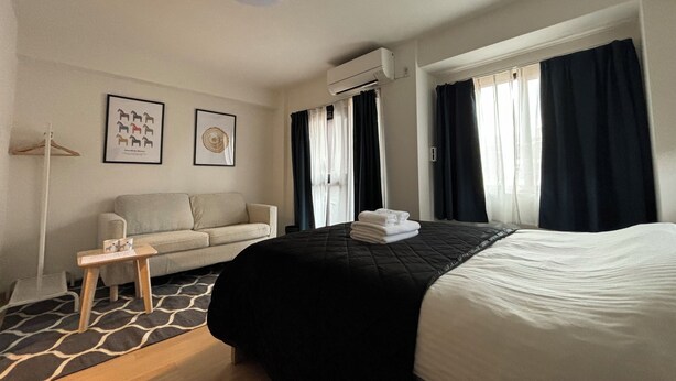 A hotel room with a bed, a sofa, a small table, and two framed pictures on the wall.