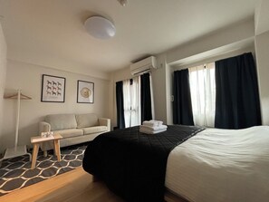 A hotel room with a bed, a sofa, a small table, and two framed pictures on the wall.