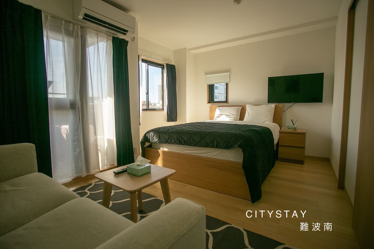 Ein Hotelzimmer mit Bett, Nachttisch, Stuhl und einem an der Wand befestigten Fernseher.