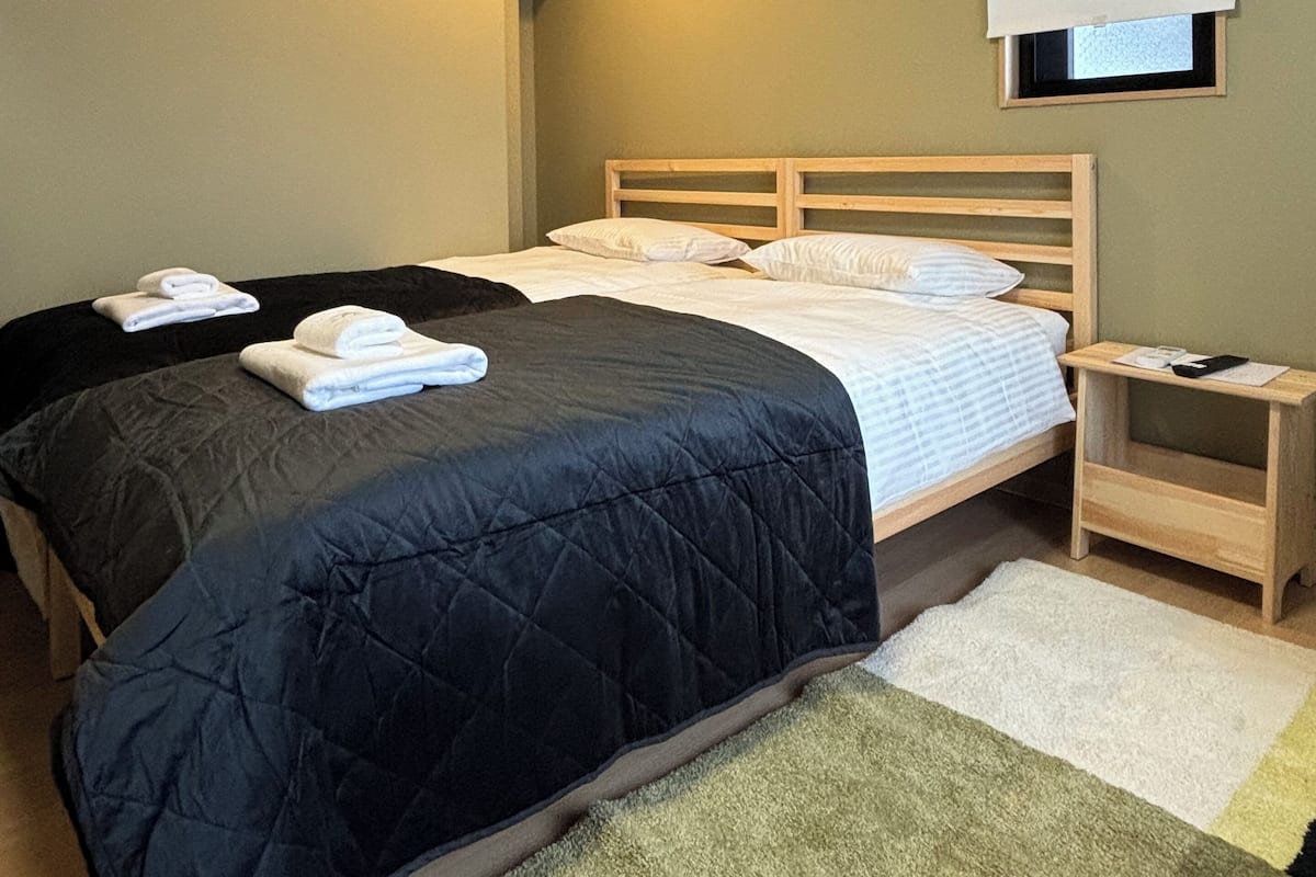 Ein Schlafzimmer mit Bett, Nachttisch, Fenster mit Jalousie und Deckenleuchte.