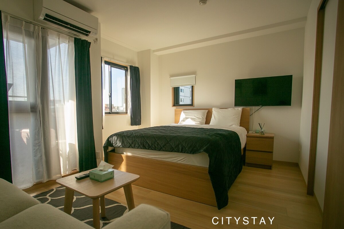 Une chambre d’hôtel équipée d’un lit, d’une table de chevet, d’une chaise et d’un téléviseur fixé au mur.