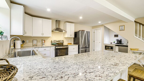 A modern kitchen with white cabinets, a granite countertop, stainless steel appliances, and a small dining area with a wooden table. - Waterfront Escape in Cub Run w/ Deck & Hot Tub! (Cub Run)