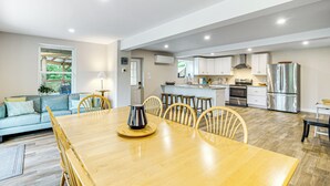 A modern kitchen with stainless steel appliances, a dining area with a wooden table and chairs, and a living area with a sofa and a window overlooking a garden. - Waterfront Escape in Cub Run w/ Deck & Hot Tub! (Cub Run)