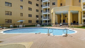 A swimming pool surrounded by a building with multiple balconies and a covered seating area. - Waterfront Biloxi Condo: Gulf-view Balcony! (Biloxi)