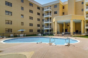A swimming pool surrounded by a building with multiple balconies and a covered seating area. - Waterfront Biloxi Condo: Gulf-view Balcony! (Biloxi)