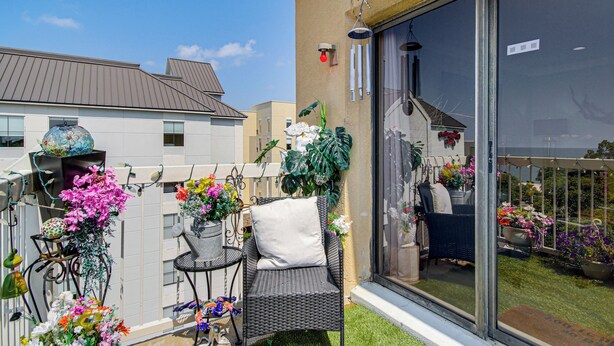 A balcony with a wicker chair, a small table, and potted plants. - Waterfront Biloxi Condo: Gulf-view Balcony! (Biloxi)