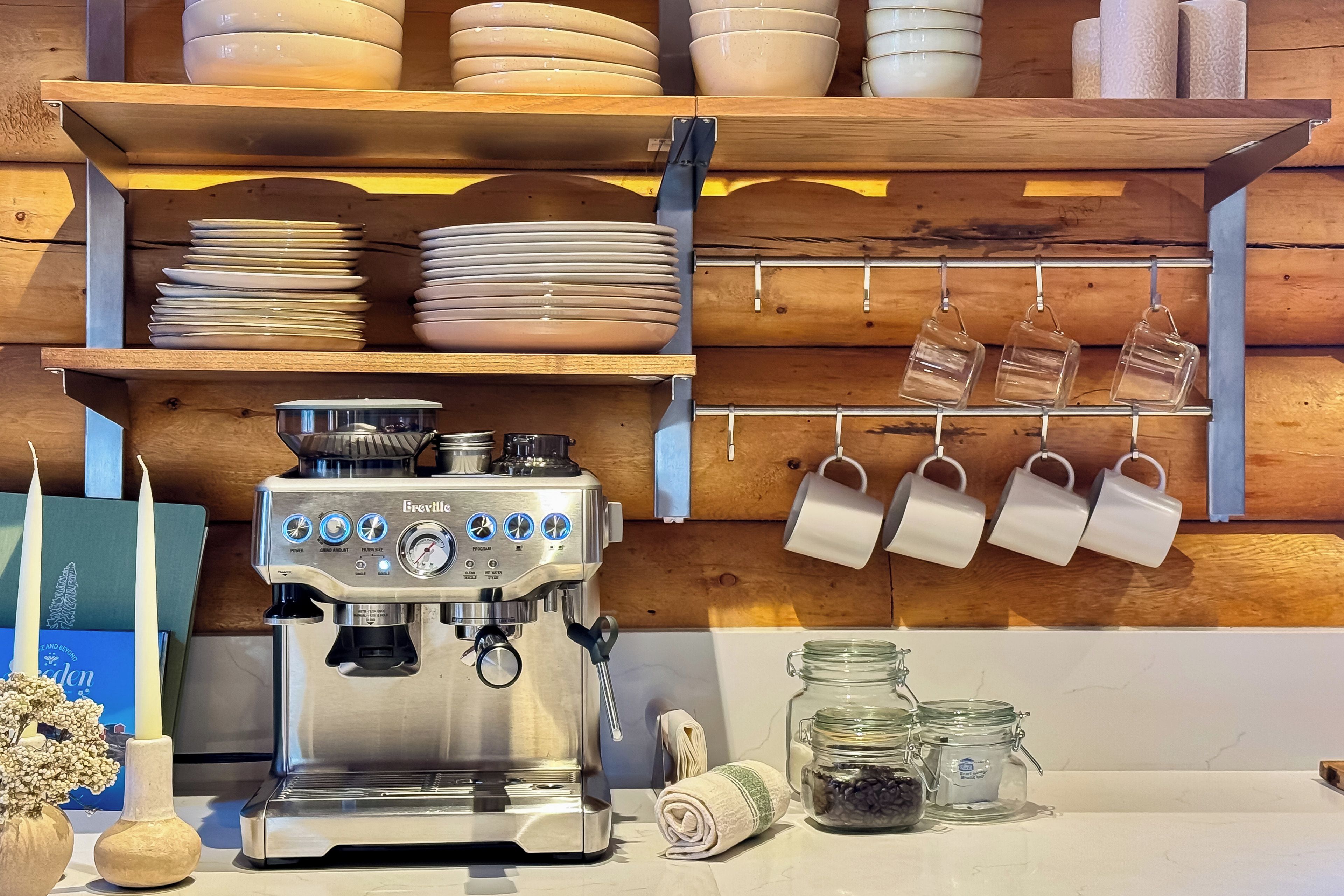 A kitchen with a Breville espresso machine, shelves with plates and mugs, and jars on the counter.