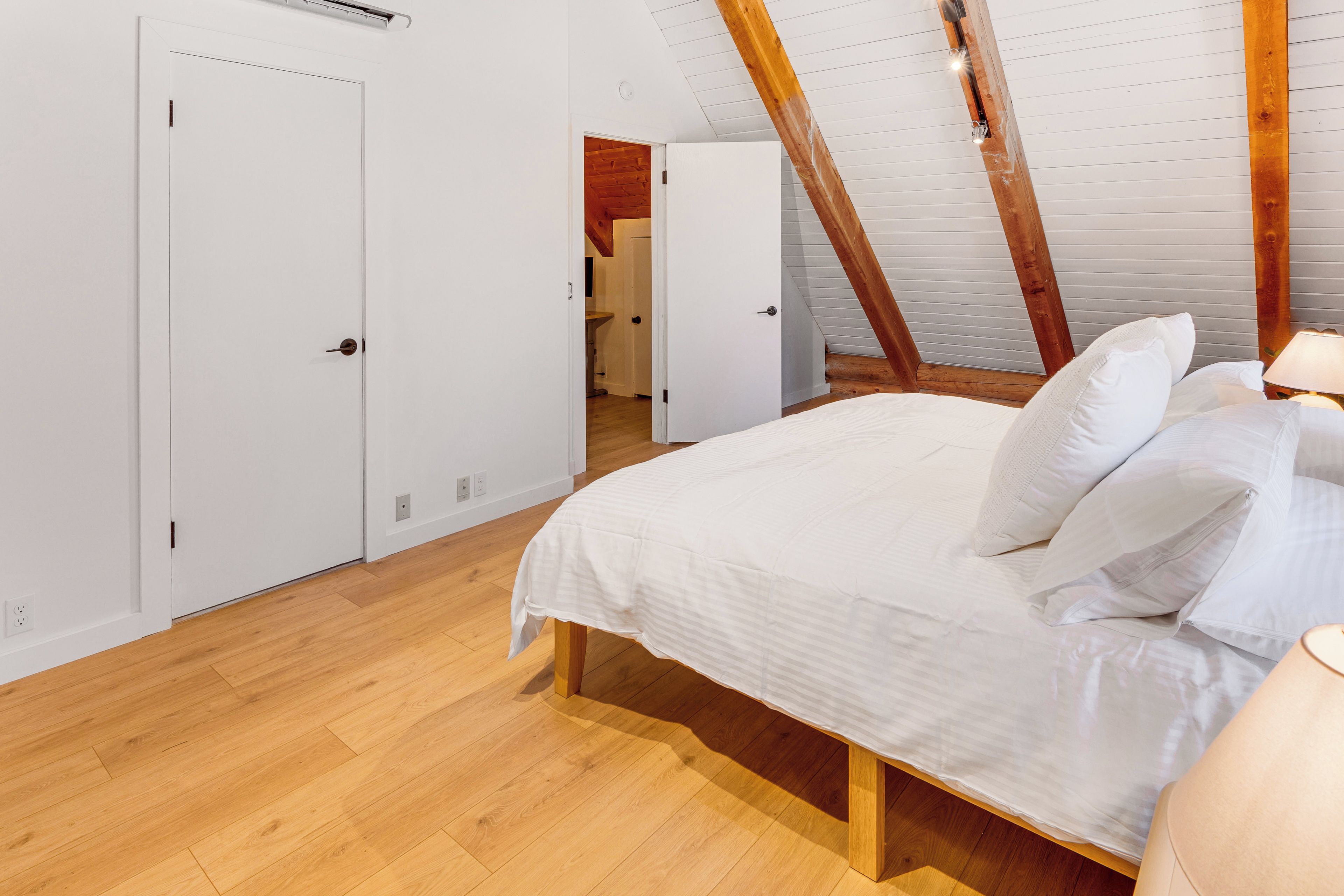 A bedroom with a wooden ceiling, a bed with white bedding, and a nightstand with a lamp.
