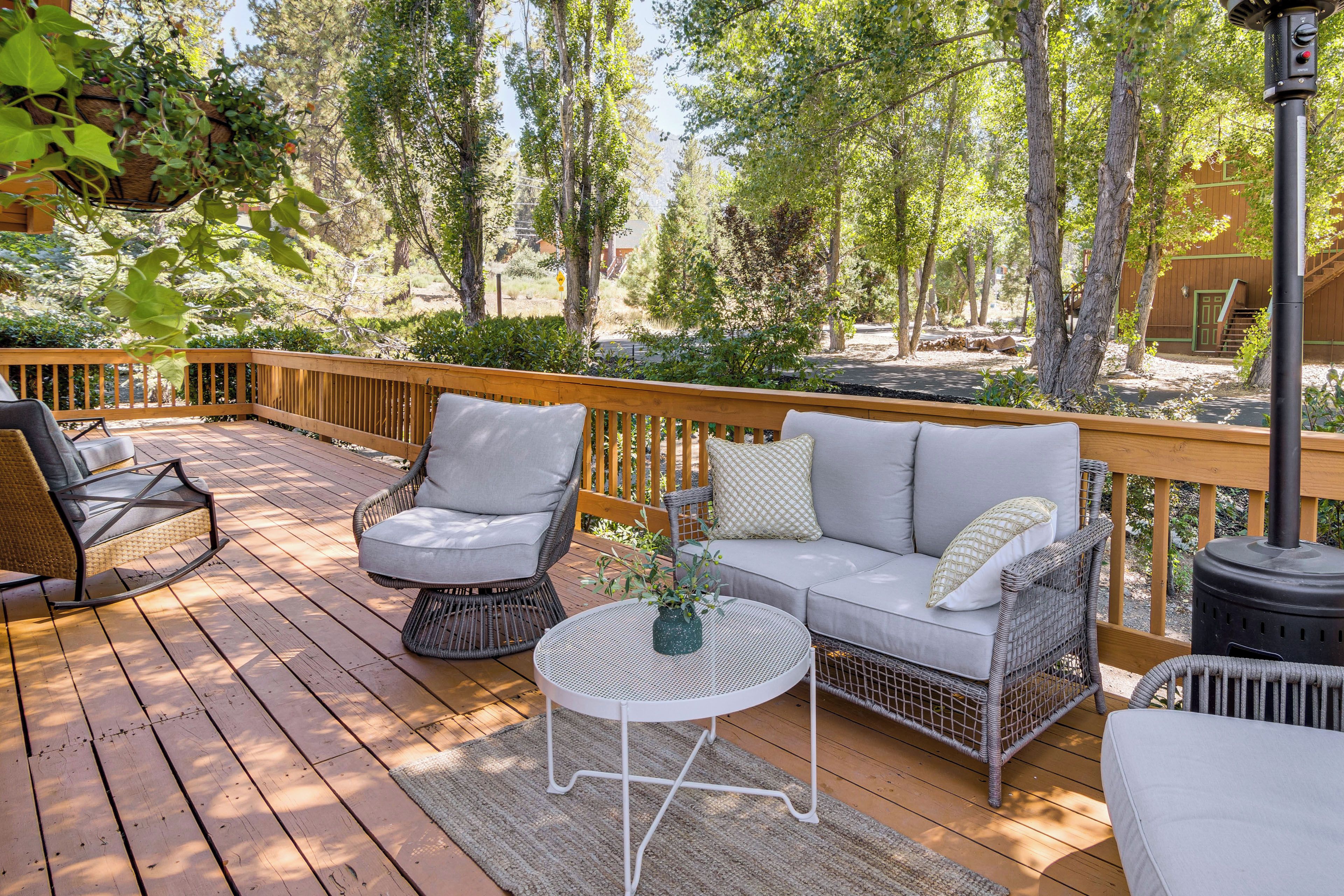 A wooden deck with wicker furniture, a white table, and a view of trees and a building in the background.