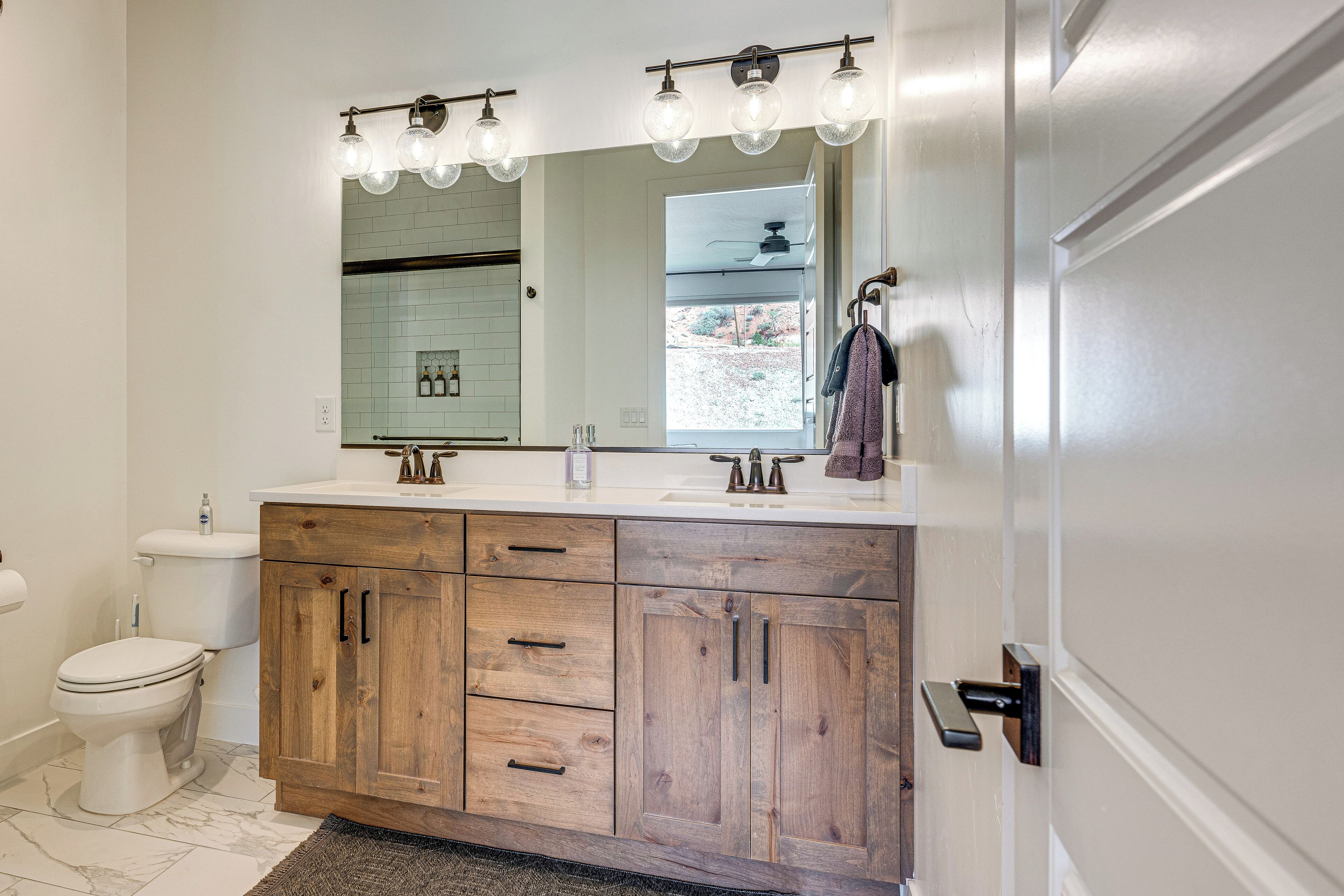 A bathroom with a wooden vanity, a white sink, and a large mirror with light fixtures.