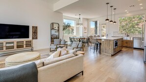 Een ruime woonkamer met een grote televisie, een bank en een eethoek, met een keuken op de achtergrond.