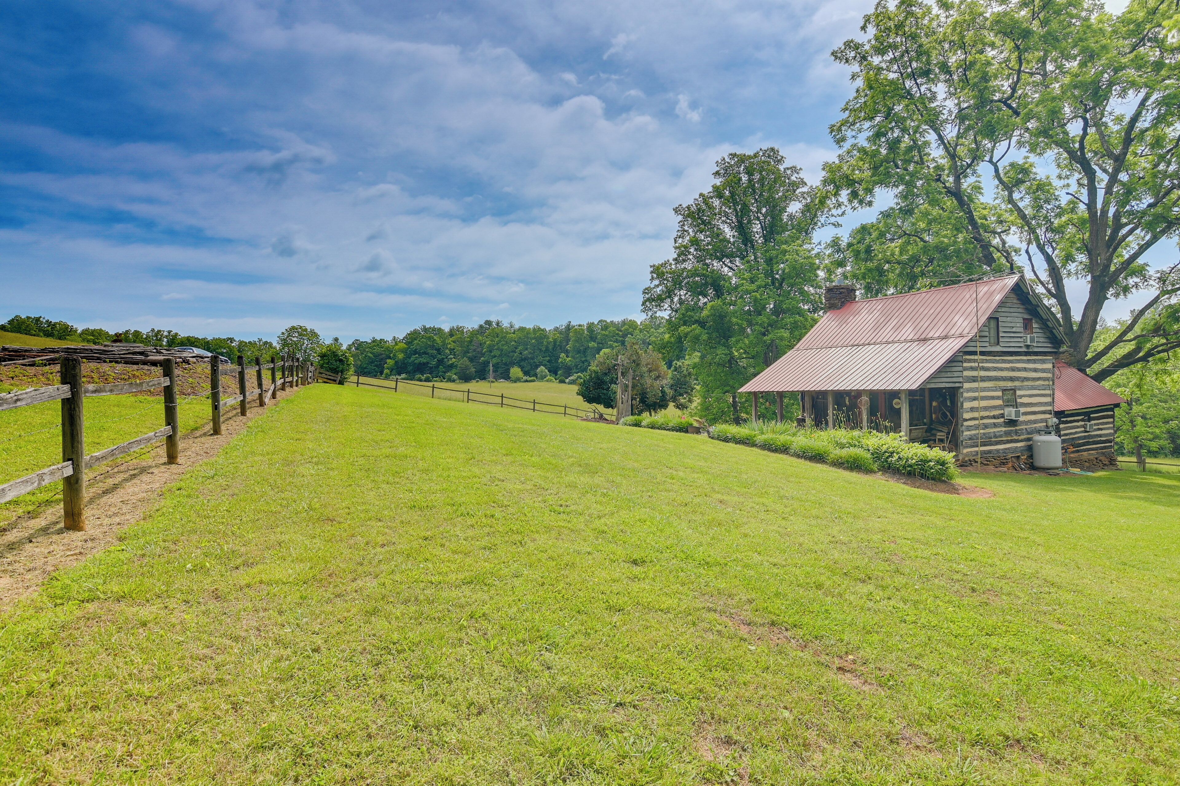 A rustic log cabin with a metal roof, surrounded by a grassy field and trees.
