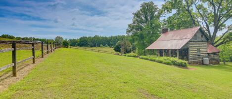 A rustic log cabin with a metal roof, surrounded by a grassy field and trees.