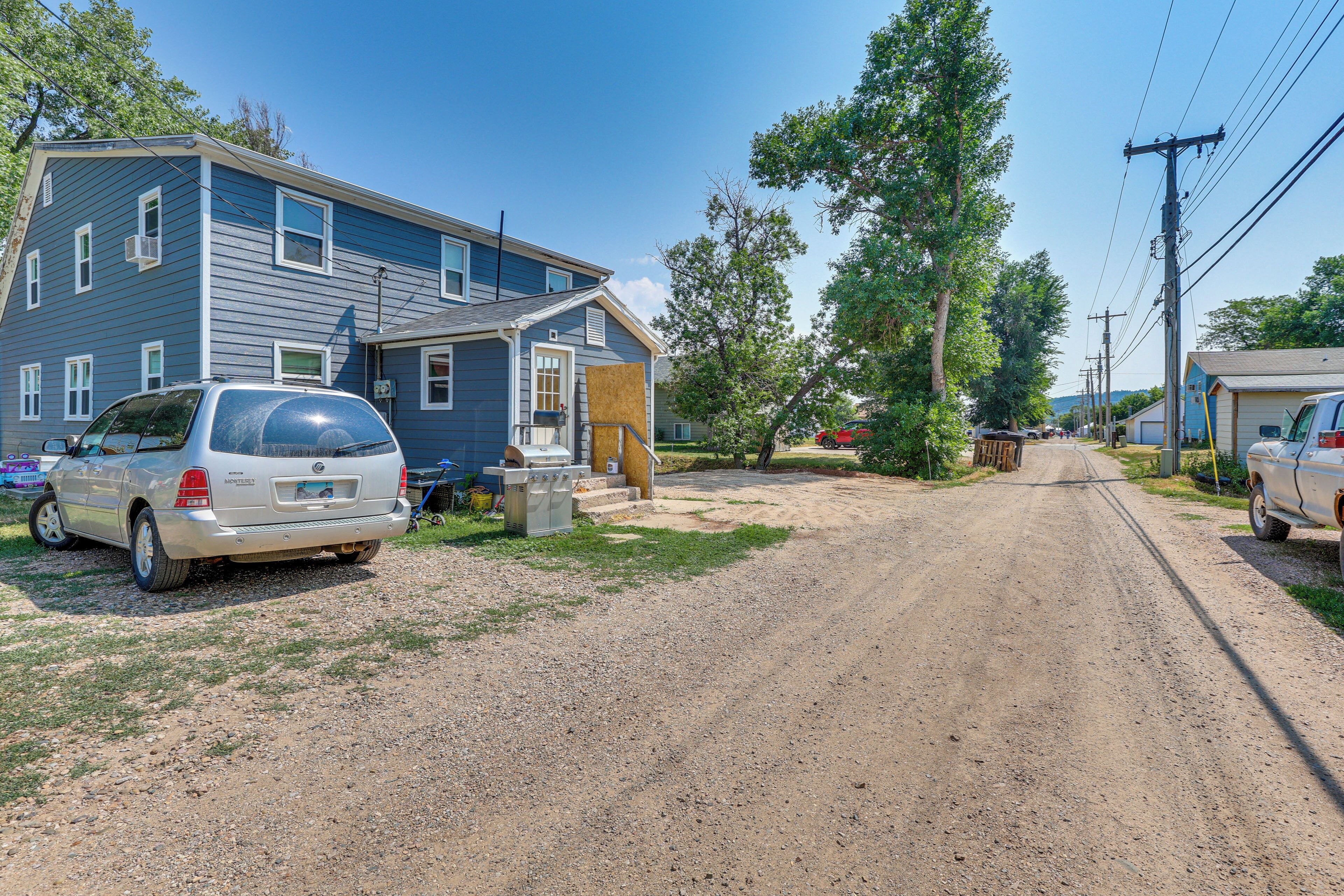 A residential area with a dirt road, houses, and parked cars.