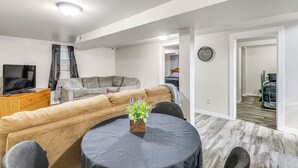 A modern living room with a sofa, a coffee table, a TV, and a clock on the wall. - Cozy Sturgis Retreat - Walk to Main St & Saloons! (Sturgis)