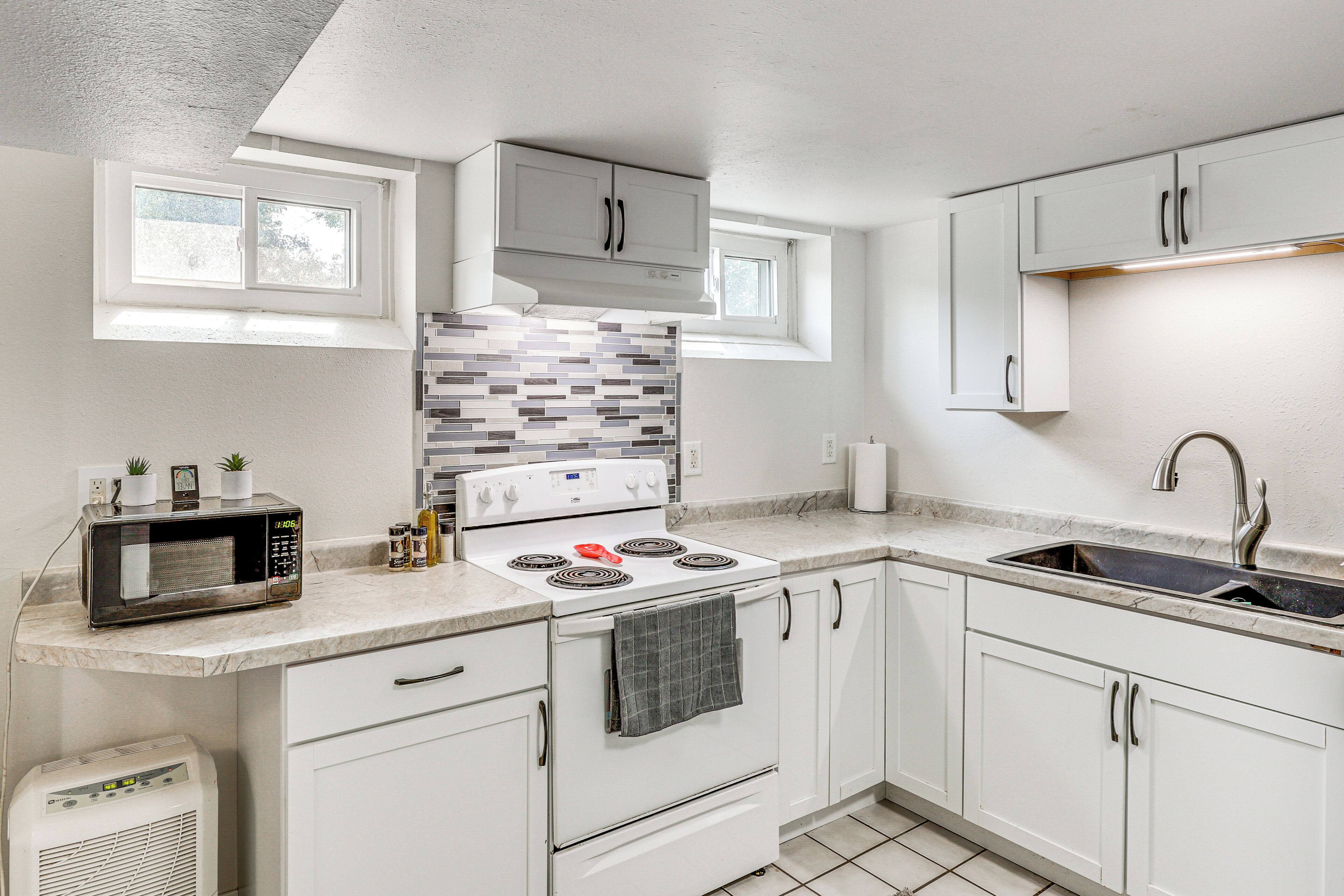 A modern kitchen with white cabinets, a built-in microwave, a stove, and a sink.