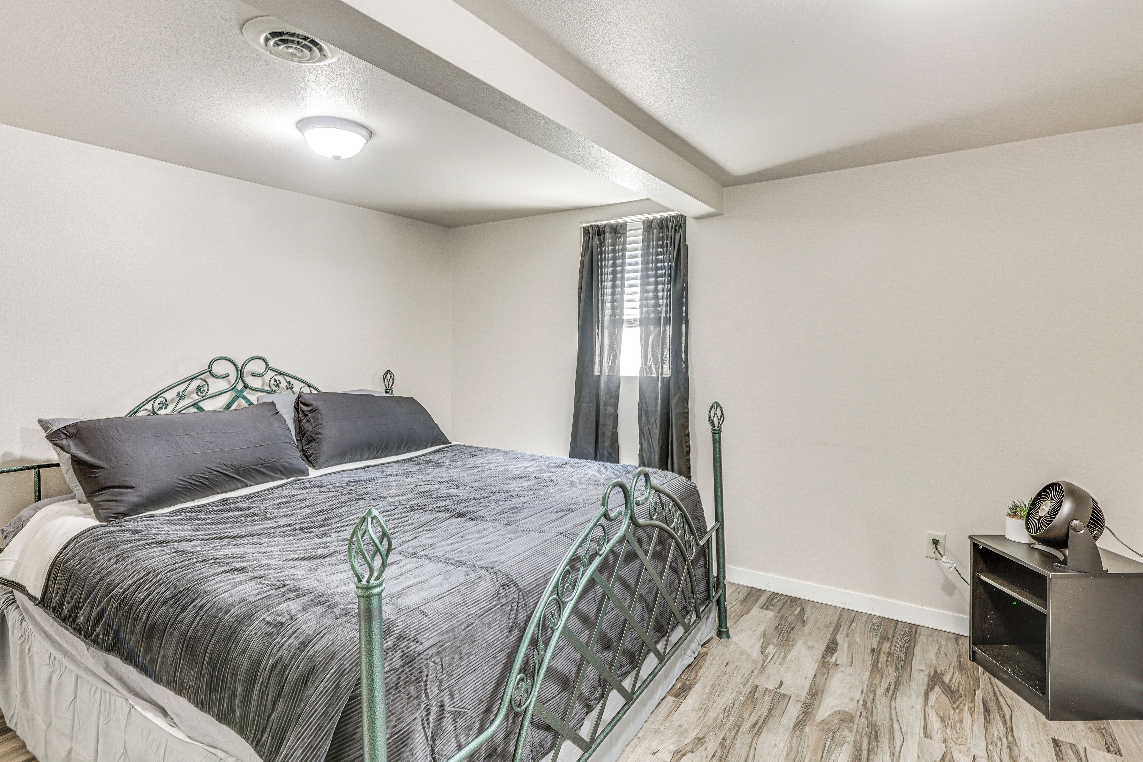 Une chambre à coucher avec un lit, une table de chevet, une étagère fixée au mur et une fenêtre avec des rideaux.